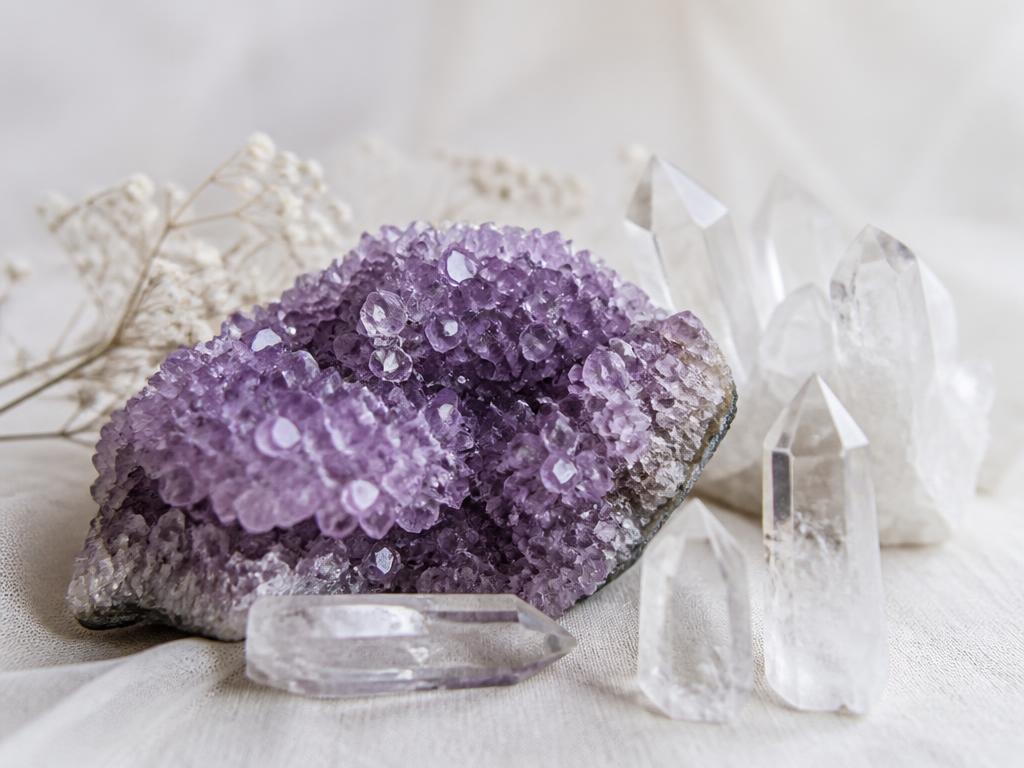A bright amethyst crystal cluster beside clear quartz points in soft daylight