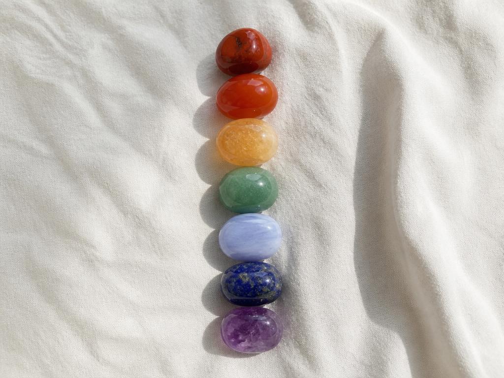 Seven chakra stones laid in rainbow order on white linen in daylight